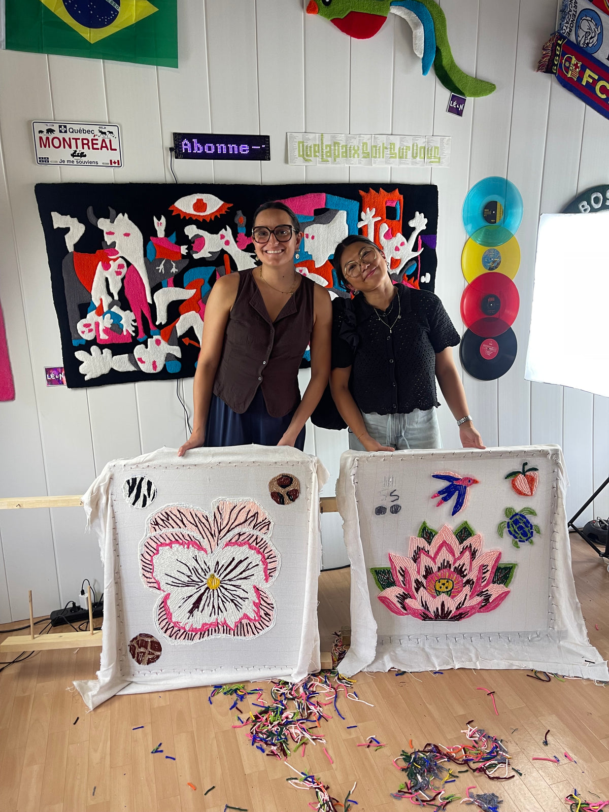 Deux participantes souriantes posant avec leurs toiles tuftées de fleurs, une pensée et un lotus, à la fin de leur initiation dans l'atelier Signé Léon à Toulouse.