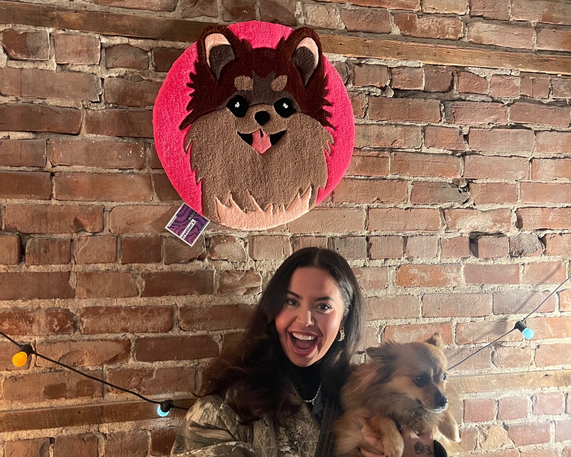 Une cliente de Mood Creations avec son chien qui pose fièrement aux cotés de son tapis personnalisé qui représente le portrait de son même chien