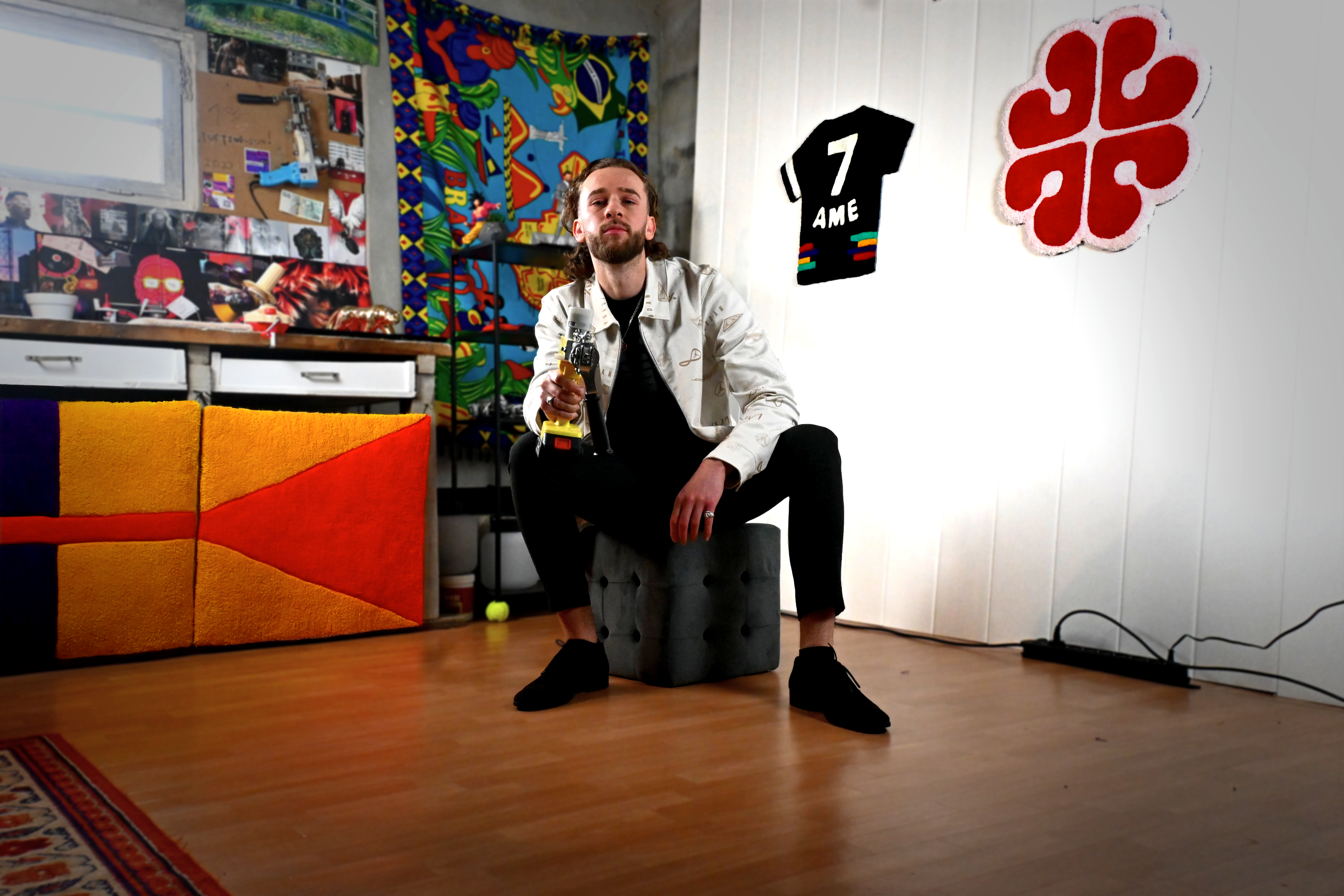 Portrait de l'artisan créateur Nathan de Signé Léon posant avec son tufting gun dans son atelier, entouré de ses tapis personnalisés et décorations murales colorées.