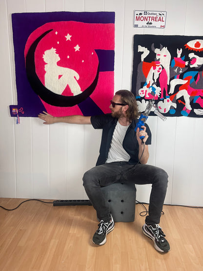 Artisan créateur Signé Léon présentant son grand tapis mural original Léon avec un pistolet à tufter dans son atelier.