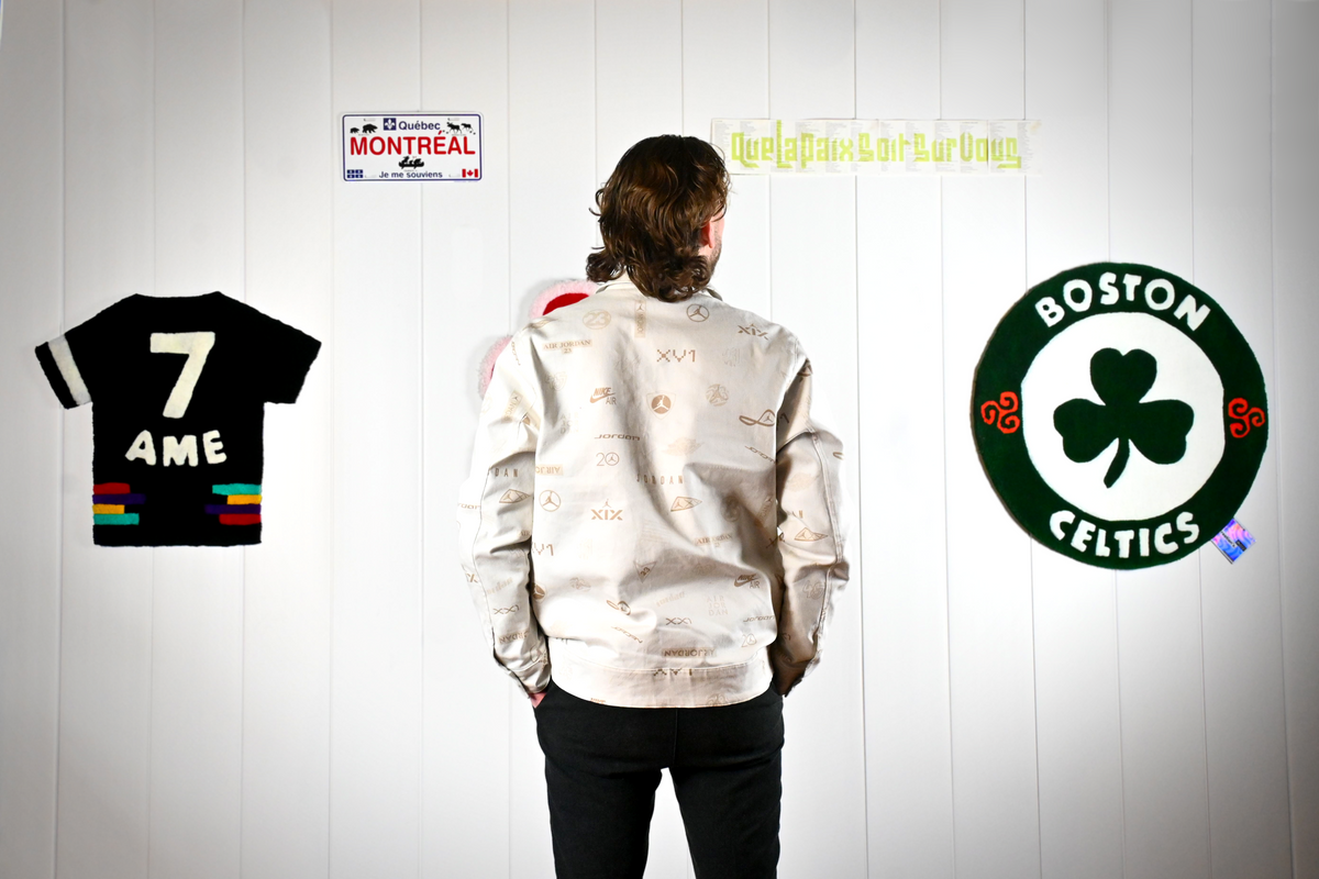 L'artisan créateur Signé Léon de dos observant ses tapis muraux personnalisés tuftés à la main, symbolisant un logo Boston Celtics et un maillot de sport.