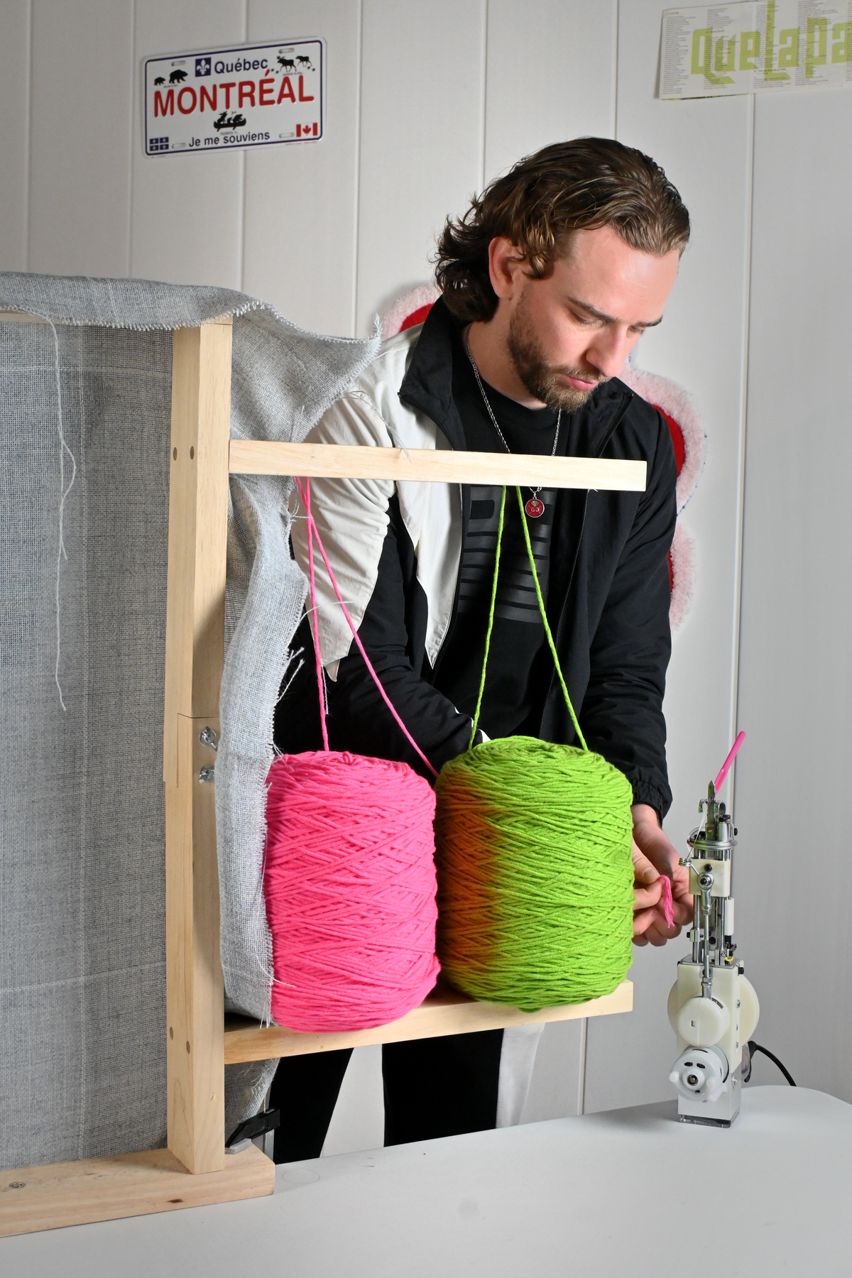 L'artisan créateur de Signé Léon concentré dans son atelier, installant ses fils de laine rose et verte fluo sur son cadre de tufting avant de démarrer une nouvelle œuvre textile.