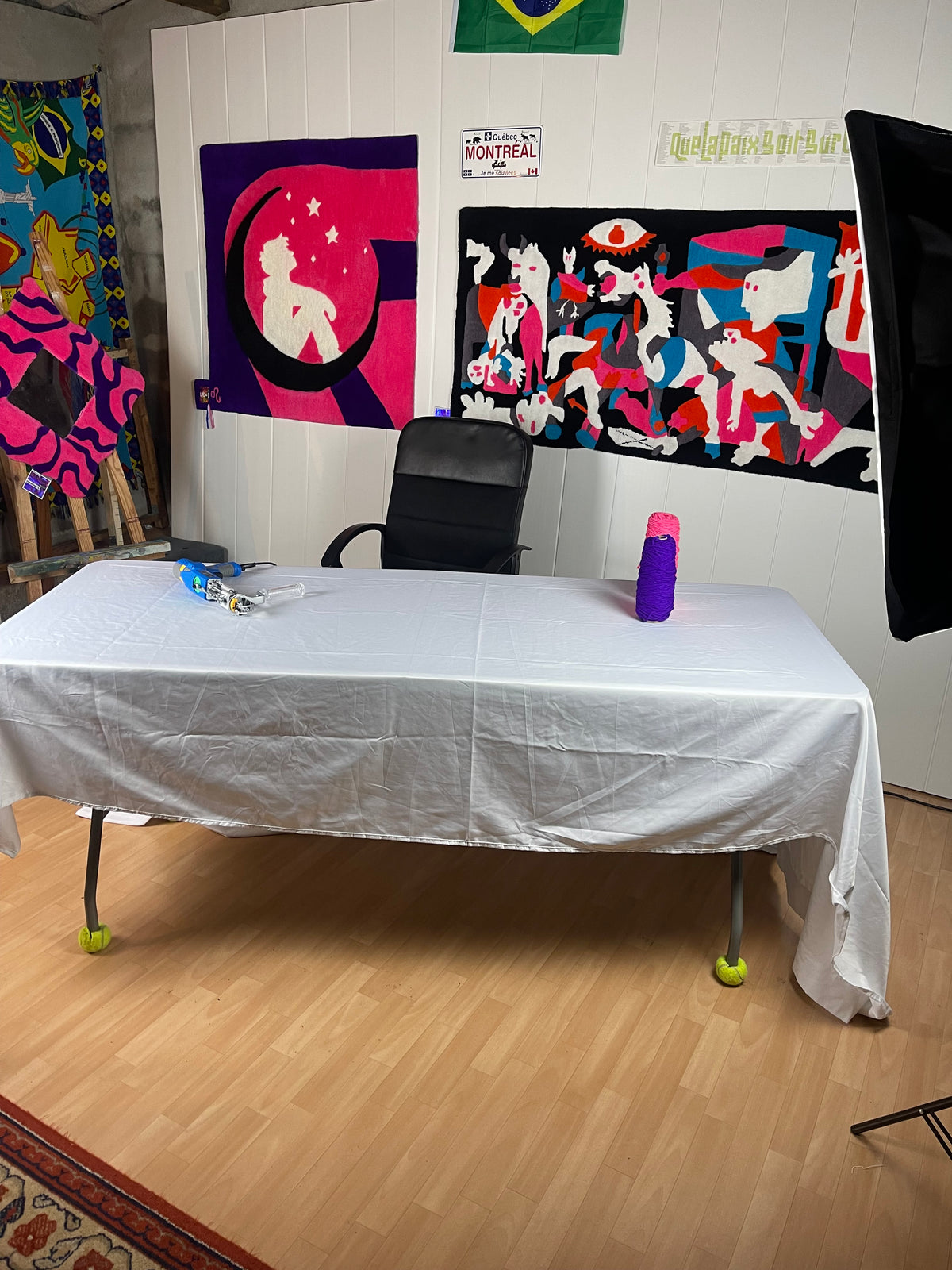 Espace de travail dans l'atelier de tufting Signé Léon, avec un tufting gun sur la table et un mur décoré de grands tapis muraux originaux colorés.