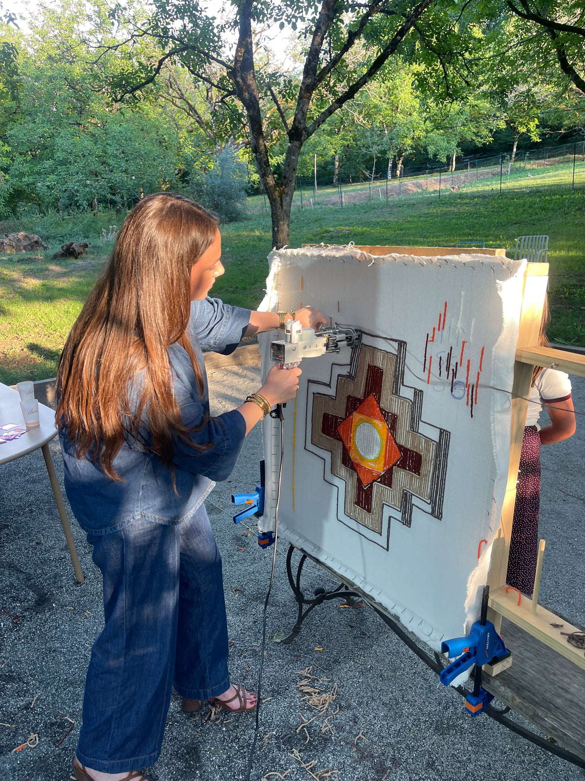 Femme réalisant un tapis tufté aux motifs géométriques en plein air lors d'une initiation au tufting directement à son domicile.