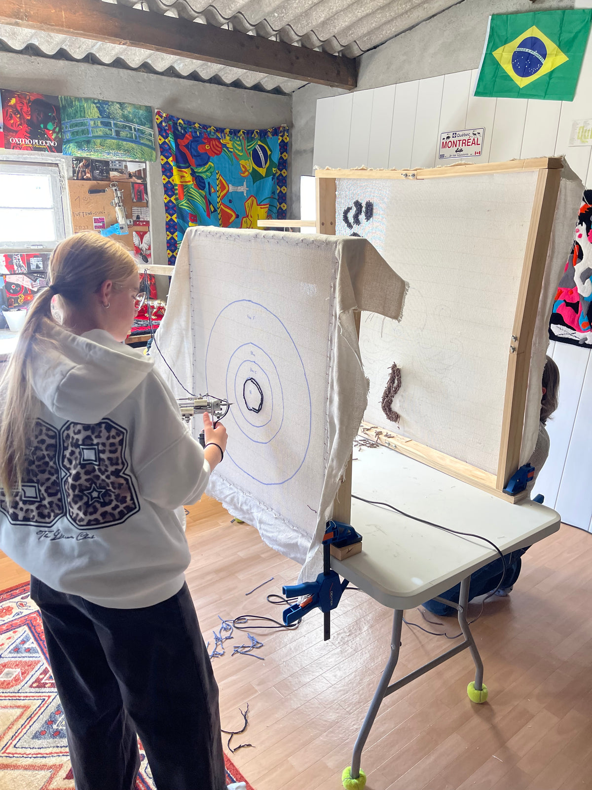 Une cliente concentrée maniant un tufting gun sur une toile aux motifs circulaires lors d'une session d'initiation à la création de tapis dans l'atelier toulousain Signé Léon.