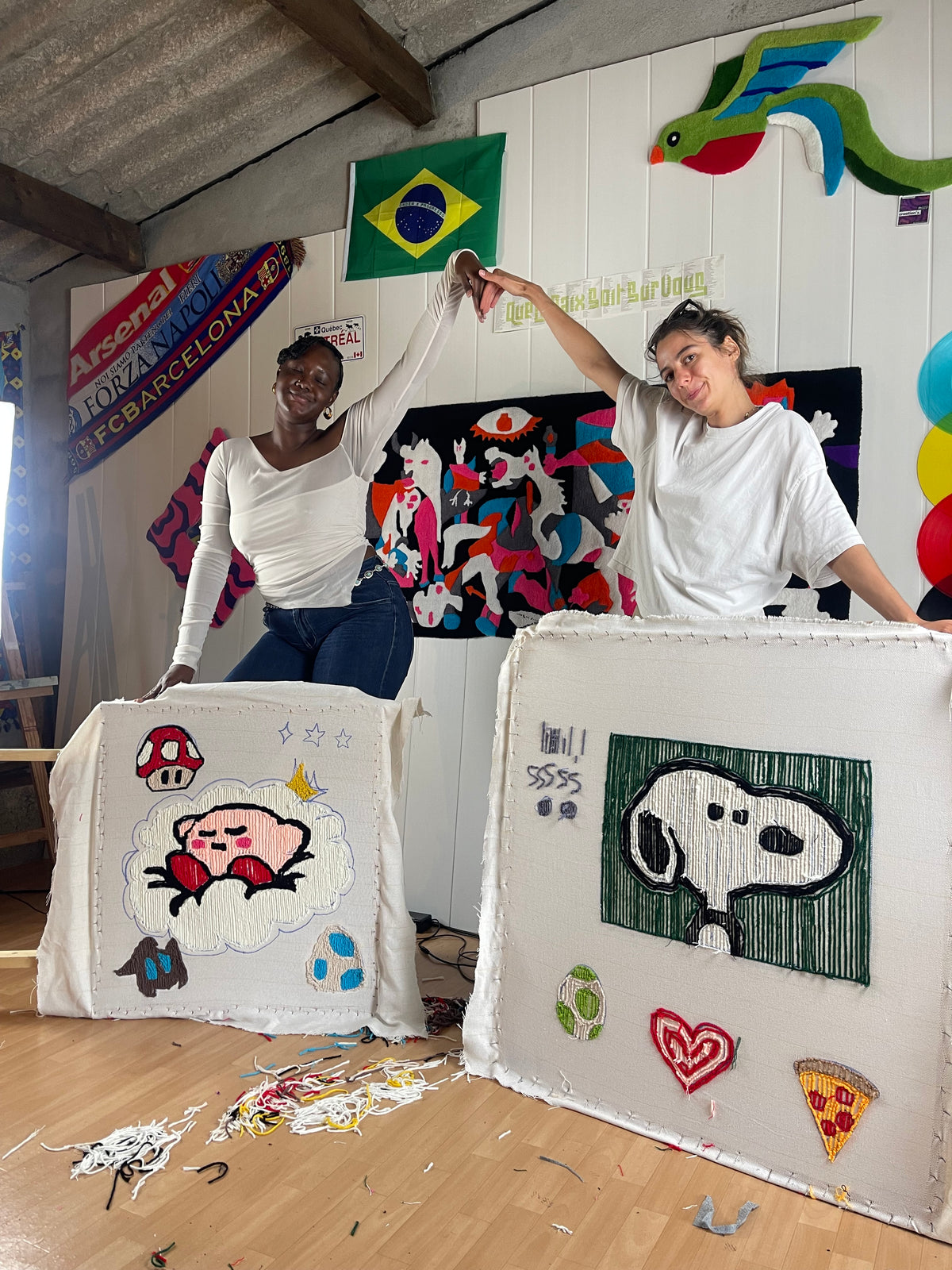 Deux clientes souriantes posant fièrement derrière leurs cadres de tufting avec leurs créations textiles terminées, représentant Kirby et Snoopy, à la fin d'un atelier d'initiation Signé Léon.