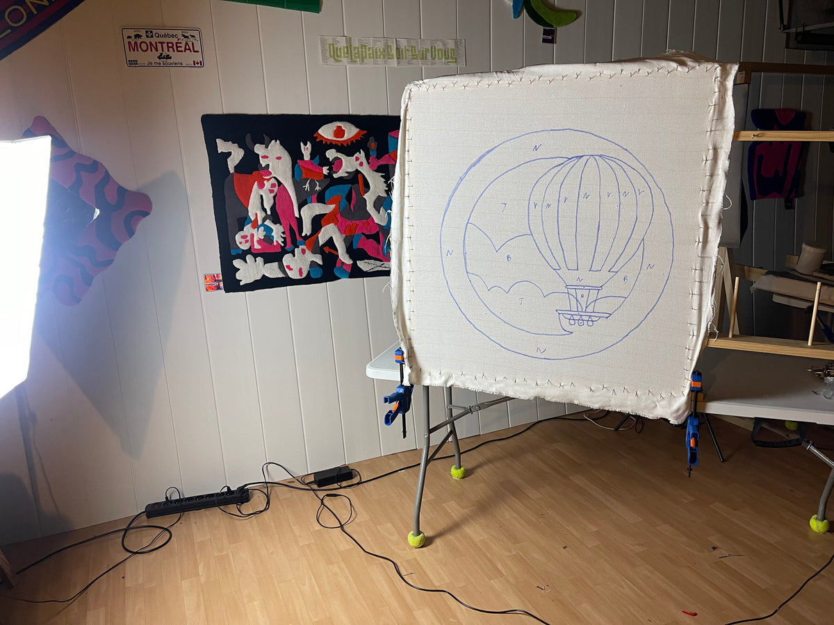 Une commande personnalisée de tapis en cours de fabrication dans l'atelier Signé Léon, montrant le dessin précis d'une montgolfière tracé sur la toile tendue avant le tufting.