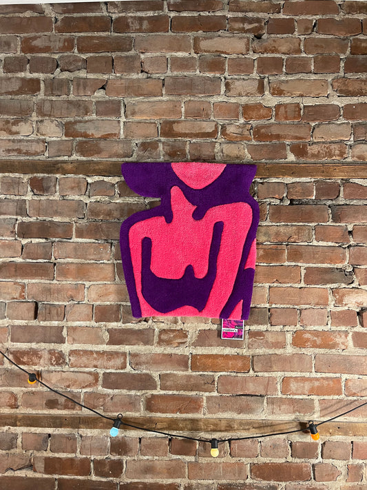 Le tapis mural tufté Alien Girl vu de face, exposé comme un tableau textile sur un mur en briques pour sublimer un intérieur.