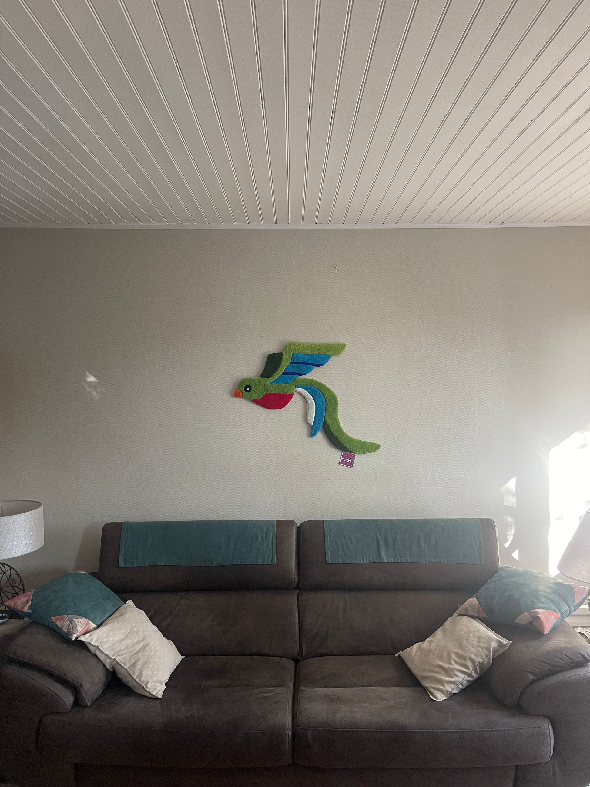 L'œuvre textile Quetzal accrochée au mur comme décoration au-dessus d'un canapé, tapis tufté oiseau tropical Signé Léon.