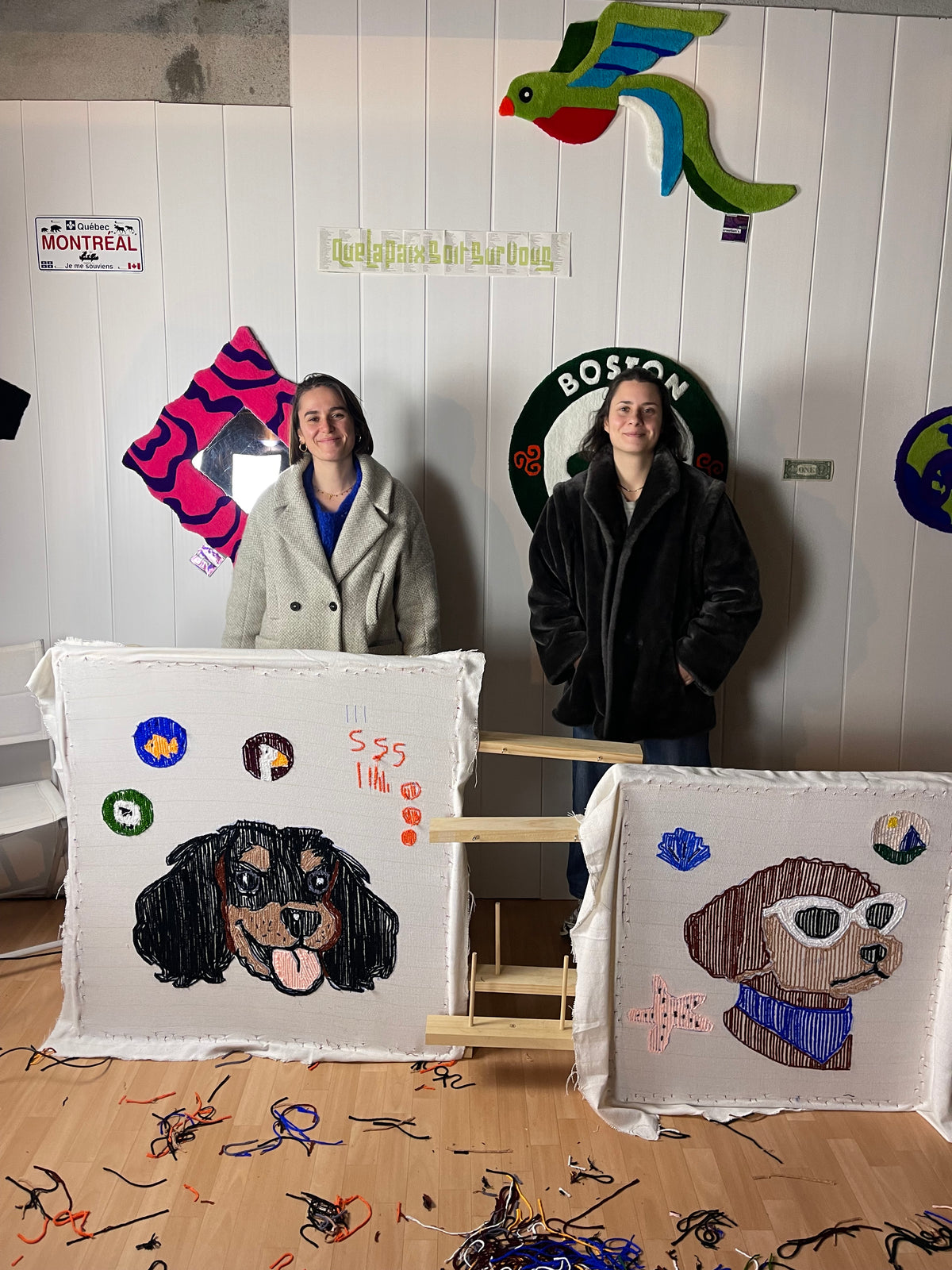 Deux participantes à l'atelier Signé Léon près de Toulouse posant avec leurs tapis tuftés en forme de portraits de chiens.
