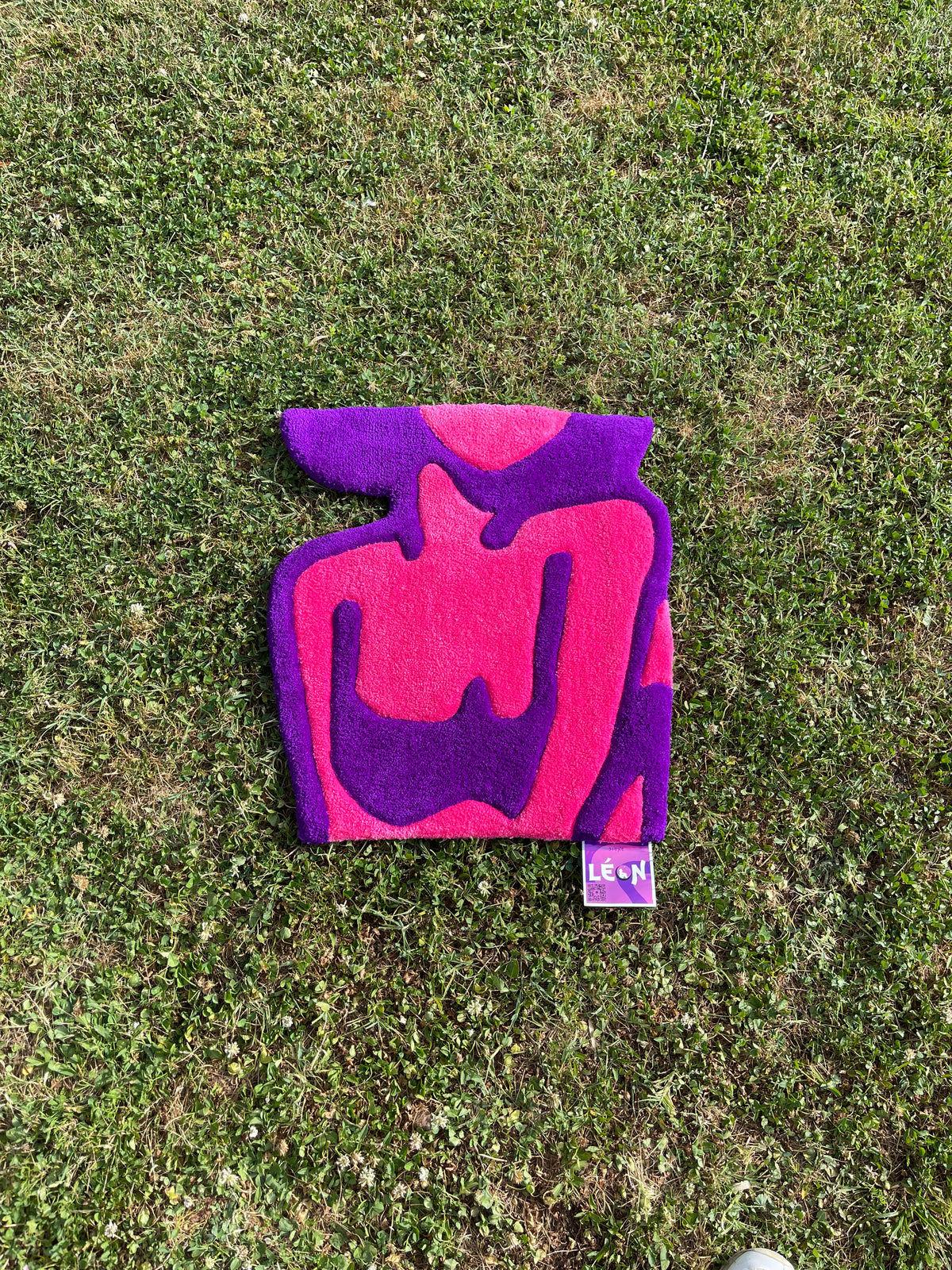 Vue de face du tapis mural Alien Girl, un buste de femme abstrait tufté à la main en rose et violet, posé sur une pelouse verte.