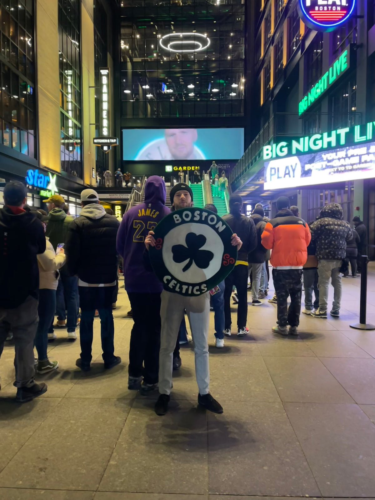 Le tapis tufté main à l'effigie des Boston Celtics brandi fièrement par son créateur dans une rue animée la nuit.